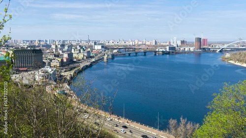 Timelapse. Picturesque view of Kyiv with car traffic, Dnieper river, numerous bridges, historical buildings and modern high-rises under clear blue sky in spring