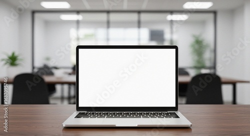 Front view of a laptop with a blank white screen on a wooden table in an office, with a blurred background.	