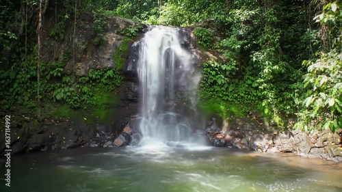 Majestic Waterfall Flows Among Lush Tropical Greens With Calm Water
