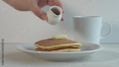 シンプル背景のホットケーキに白いピッチャーからシロップをかける
