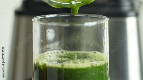 Pouring vibrant green smoothie into a clear glass cup with a blurred background setting scene