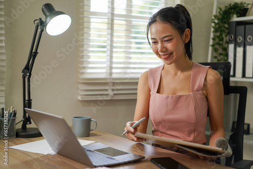 A woman is sitting at a desk with a laptop and a pen