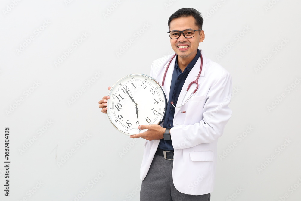 Asian adult male doctor standing, wearing doctor's coat, stethoscope on neck, isolated on white background, carrying wall clock, smiling expression, showing time or alarm. Asian adult male doctor standing, wearing doctor's coat, stethoscope on neck, isolated on white background, carrying wall clock, smiling expression, showing time or alarm.