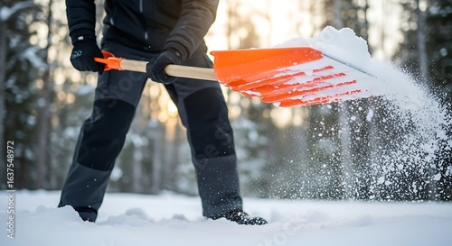 Man shoveling snow during winter season with orange snow shovel in a winter landscape providing outdoor activities after snowfall
