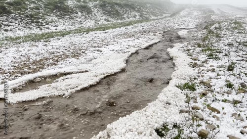Large hail flows down from the mountains after bad weather. The surrounding area is covered in white hail remnants.