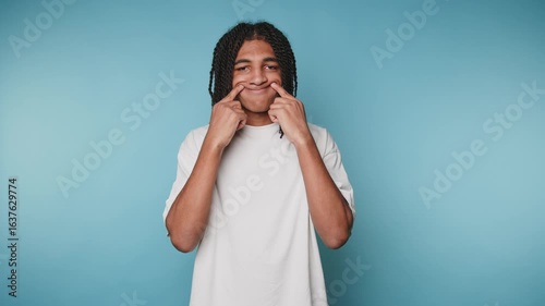 footage of young man poking his cheeks with a playful expression, showing humor and lightheartedness on light blue background