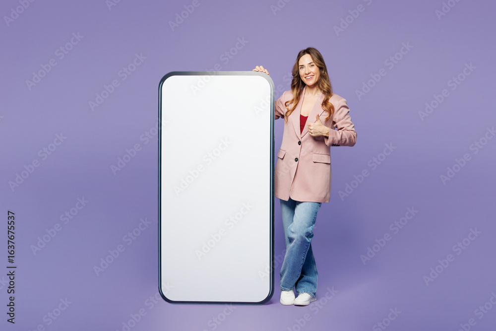 Full body young woman wear beige jacket formal clothes big huge blank screen mobile cell phone smartphone with area show thumb up isolated on plain pastel light purple background. Lifestyle concept. Full body young woman wear beige jacket formal clothes big huge blank screen mobile cell phone smartphone with area show thumb up isolated on plain pastel light purple background. Lifestyle concept.