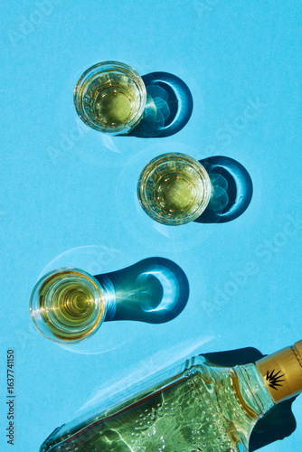 Three glasses of golden tequila placed on a blue background, with a bottle nearby, showcasing reflections and shadows, creating a vibrant and inviting atmosphere for beverage enjoyment
