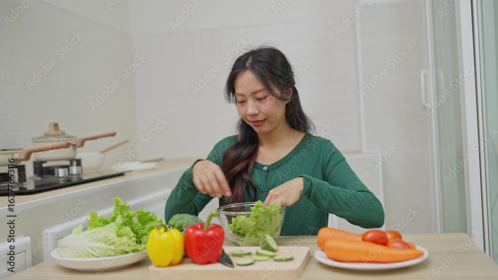 Young woman preparing fresh vegetables in bright kitchen with colorful ingredients for healthy meal, including lettuce, peppers, cucumbers, and carrots Young woman preparing fresh vegetables in bright kitchen with colorful ingredients for healthy meal, including lettuce, peppers, cucumbers, and carrots