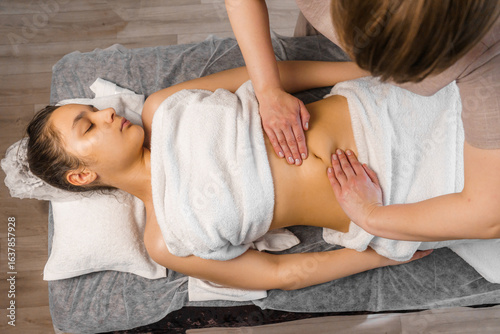 Slim young woman receiving stomach massage in spa salon.