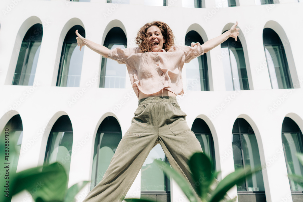 Obraz premium Happy energetic Caucasian woman jumping against the background of a building with arches.