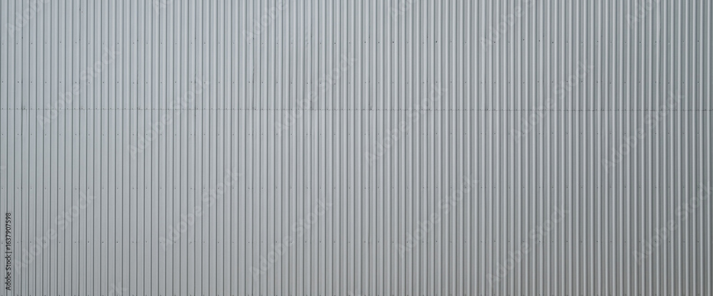 Obraz premium Corrugated metal wall texture with vertical lines reflecting natural light and shadows in an industrial setting
