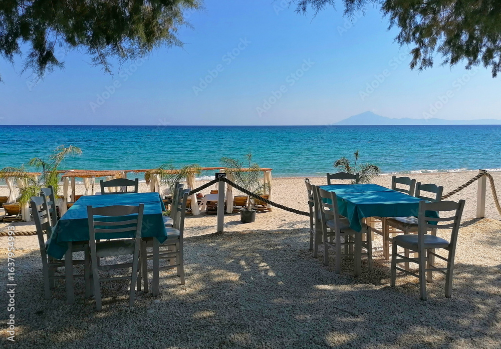 Fototapeta premium Beach restaurant on the island of Thasos, Greece stock photo images. Tables and chairs on the beach of Thassos, Greece. Beautiful beach in Limenaria resort photo images