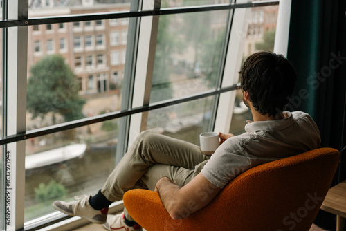 man drinking coffee in a chair with attic window and view on Amsterdam	