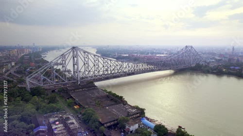 A drone aerial movement shot of the moving vehicles on the busy, iconic Howrah Bridge over the holy Ganges or Hooghly river in Kolkata or Calcutta city, India on a cloudy, rainy day