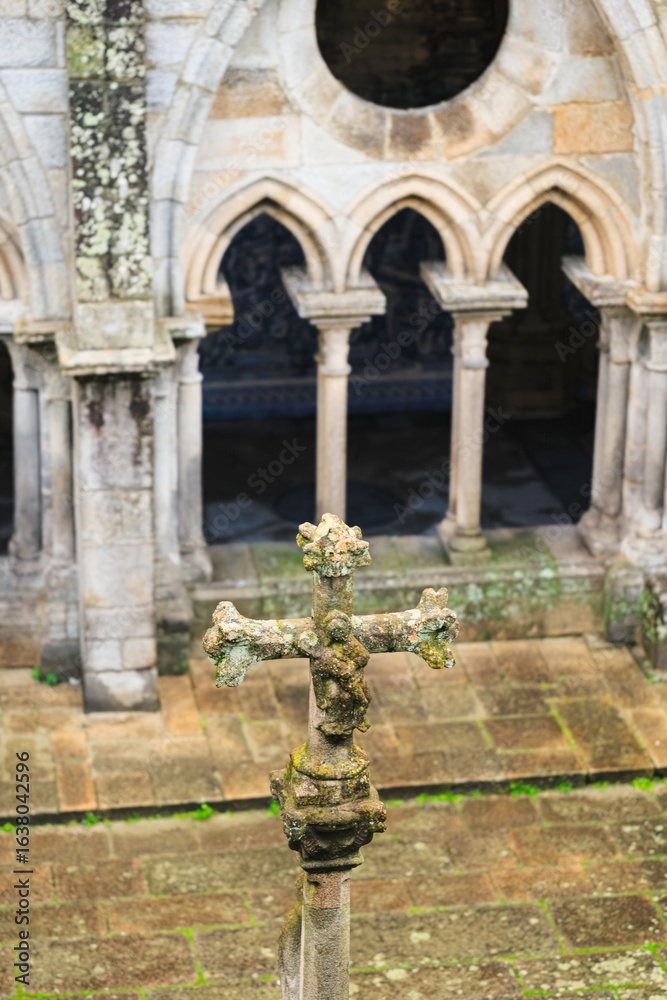 Obraz premium A moss-covered stone cross stands prominently in the foreground, overlooking the ancient cloister of Bom Jesus do Monte in Braga. Sunlight filters through arches