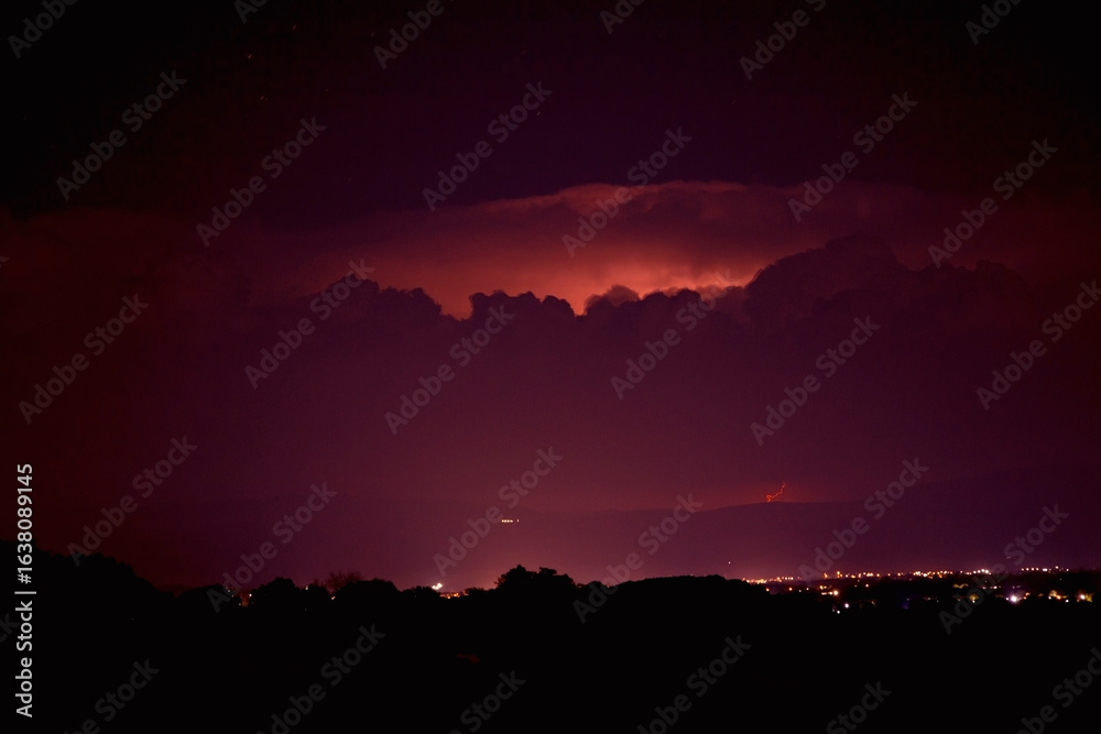 Obraz premium Night sky with heavy storm and lightning. City lights on far distance.