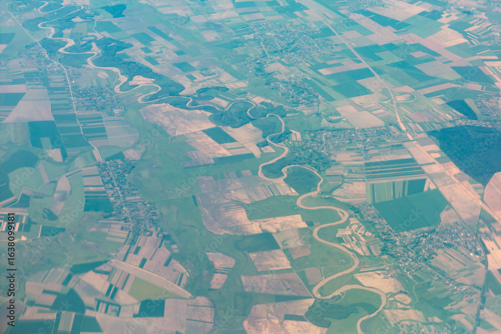 Fototapeta premium Aerial view of the Prut River winds through a patchwork of green fields in Romania and Moldova. Small settlements dot the landscape, framed by the river meandering path