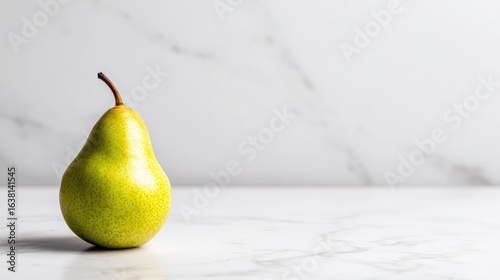 A juicy pear with smooth green-yellow skin placed off-center on a white surface
