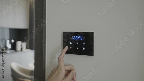 A hand adjusting a modern smart thermostat showing a temperature of 26C. Optimizing indoor climate for comfort and efficiency.