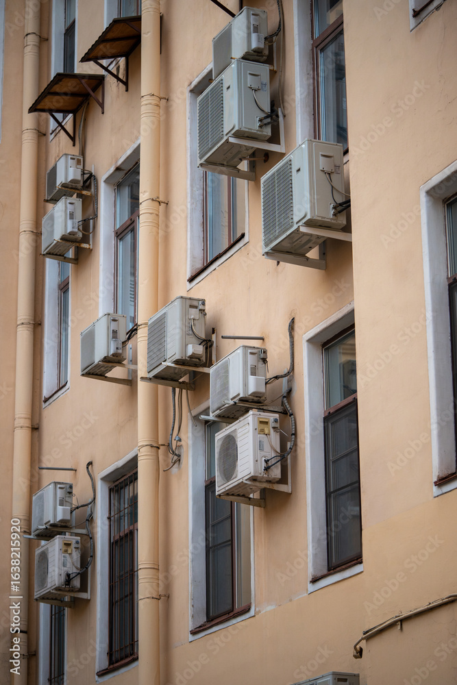 Facade of building with many air conditioners on windows in southern hot country. Yellow house exterior on city street. Escape from heat, creating favorable microclimate in urban apartments concept. Facade of building with many air conditioners on windows in southern hot country. Yellow house exterior on city street. Escape from heat, creating favorable microclimate in urban apartments concept.