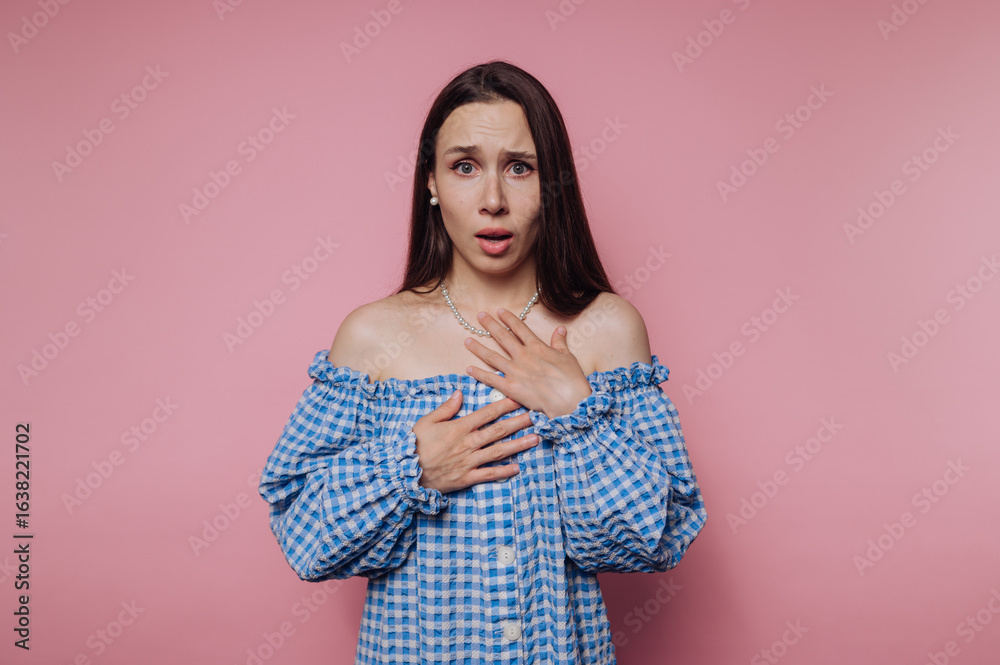Obraz premium A surprised woman in a blue checkered off-shoulder dress against a pink background.