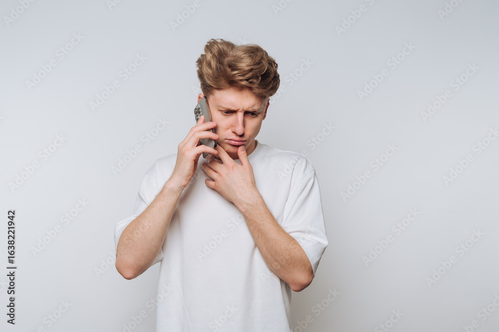 Young man in white t-shirt talking on smartphone with a concerned expression. Young man in white t-shirt talking on smartphone with a concerned expression.