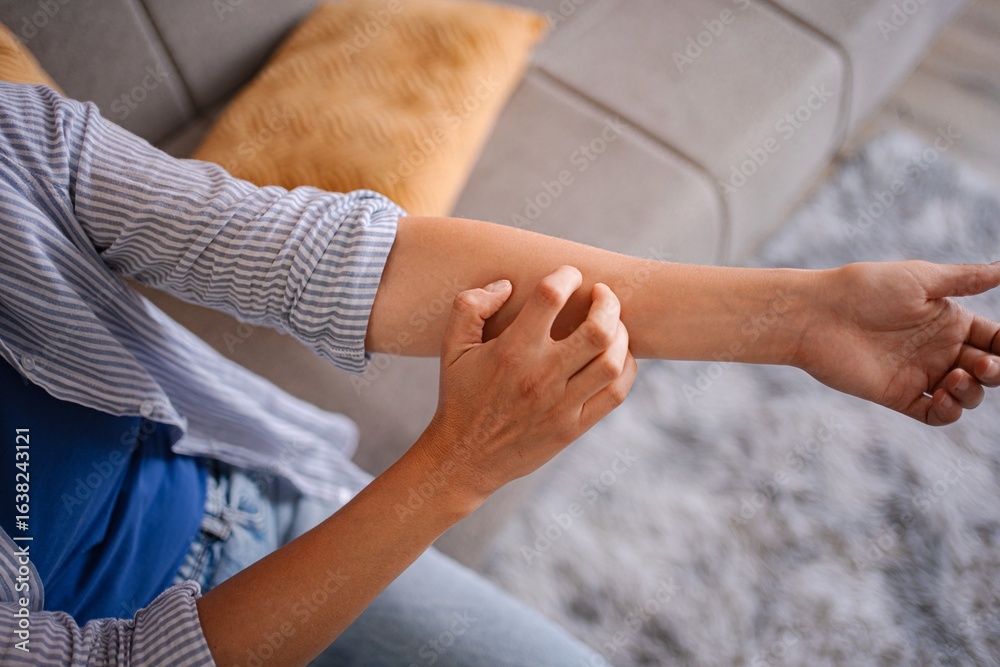 Fototapeta premium Woman scratching her itchy arm, suffering from dermatitis at home