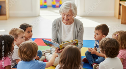 Senior woman reading a storybook to a group of diverse children sitting on a colorful rug in a bright classroom, fostering a love for reading and learning together
