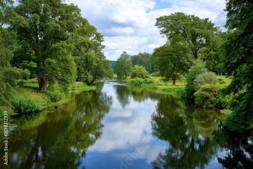 Serene river reflecting lush green trees and cloudy sky on a sunny day