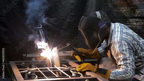Bild auf Leinwand Focused welder in helmet and gloves performing metal join with bright arc and th