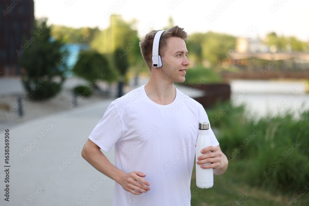 Smiling sportsman in headphones running with thermo bottle outdoors. Morning exercise Smiling sportsman in headphones running with thermo bottle outdoors. Morning exercise