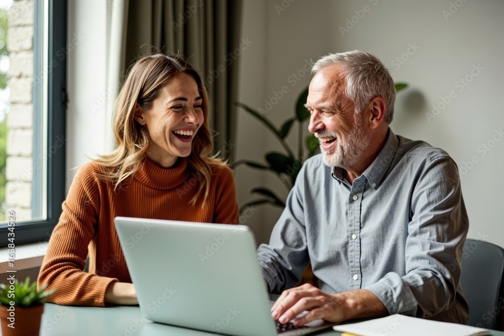 Middle-aged couple bonding over a good laugh while collaborating on a laptop in their warm home workspace. Middle-aged couple bonding over a good laugh while collaborating on a laptop in their warm home workspace.