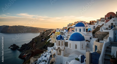 Fototapeta Naklejka Na Ścianę i Meble -  Aegean sunset over Santorini. Colorful buildings with blue domes cluster on a cliff overlooking a calm sea at golden hour