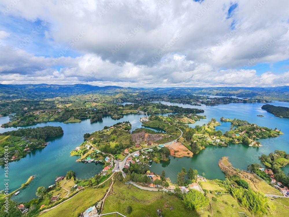 Fototapeta premium Aerial view revealing guatape's colorful landscape, featuring turquoise reservoir, verdant terrain, and rugged mountain silhouettes against dramatic colombian scenery