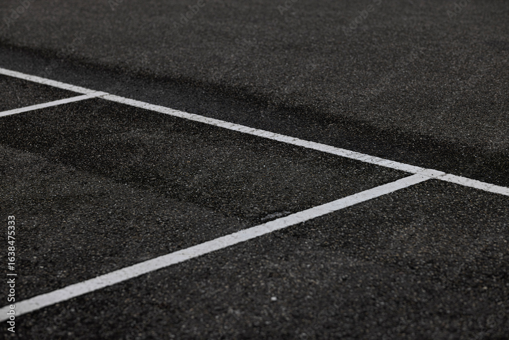 Fototapeta premium White painted lines intersecting on dark asphalt pavement creating geometric corner marking pattern