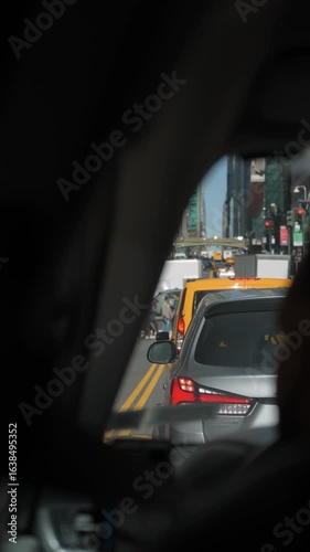 A taxis rearview mirror vividly captures a busy city traffic scene, showcasing congestion and bustling streets
