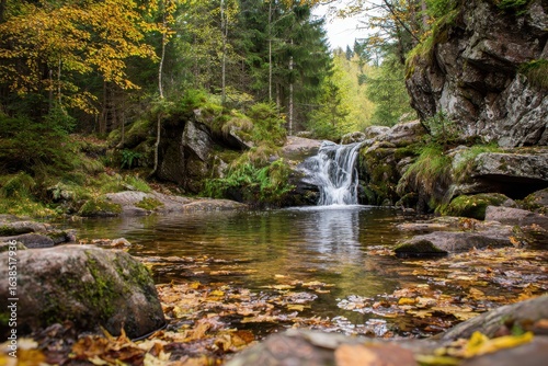 Small waterfall cascades gently in a serene forest during an autumn day, surrounded by vibrant foliage and reflective water surfaces