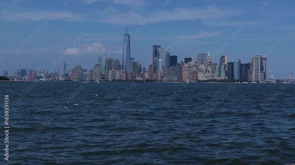 The New York City skyline rises majestically above the water on a bright day with clear blue skies The New York City skyline rises majestically above the water on a bright day with clear blue skies