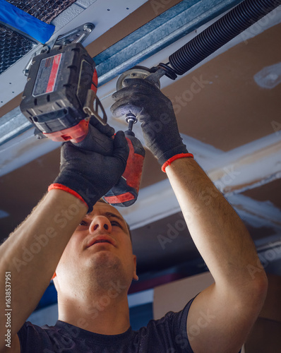 Fényképezés Low angle view of a worker fastening a spring on a garage door mechanism during installation or repair