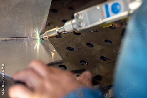 Detail of laser welding of aluminum with green flame with sparks and welding gun in hand in safety suit. Dangerous work