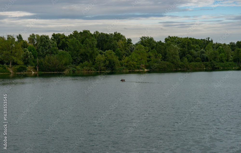Fototapeta premium Man Fishing on Boat in Countryside Lake with Forest on the Background