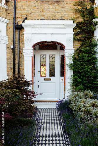 Fotografie White door with stained glass window and black and white tiled pathway leading t
