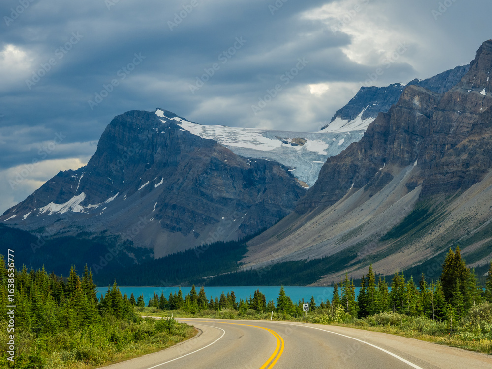 Fototapeta premium Car driving along Icefields Parkway toward towering Rocky Mountains