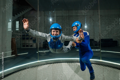 A male instructor teaches a woman how to fly in a wind tunnel. Free fall simulator.