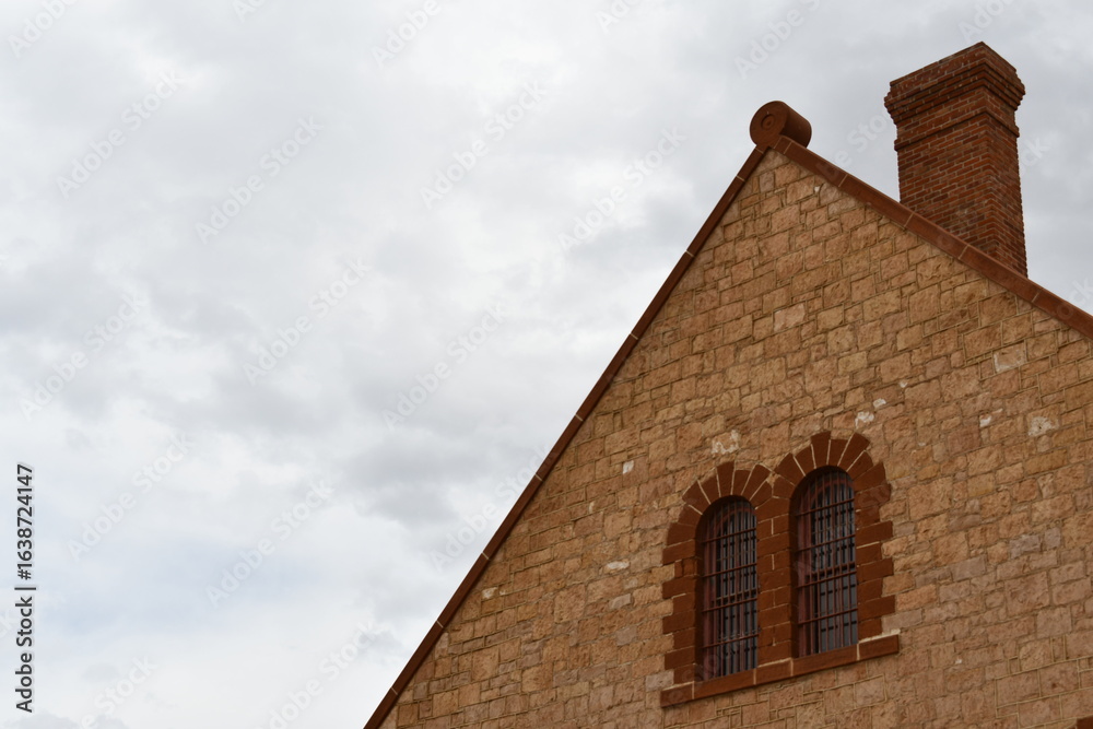 Obraz premium Large vintage prison made of stone. High roof pitch, red brick chimney. Barred windows.