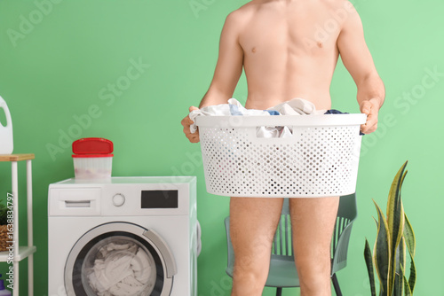Tableau sur toile Young man covering himself with laundry basket on green background