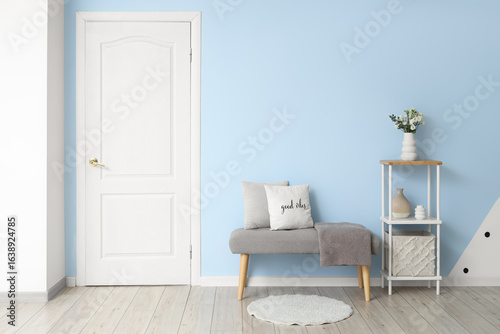 Interior of stylish hallway with grey bench, shelving unit and white door