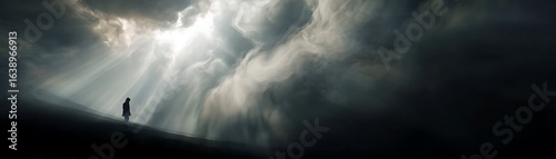 Silhouette of a person standing on a hill under a dramatic sky.