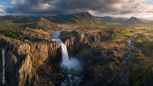A waterfall in a rocky area with a mountain range in the backgro